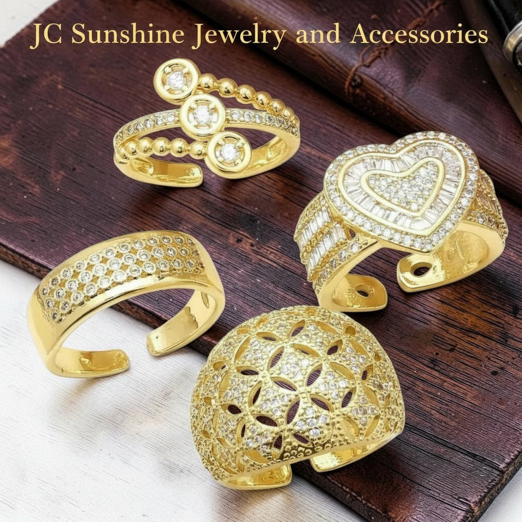 JC Sunshine Jewelry and Accessories set of four gold-plated rings with cubic zirconia. Features a heart-shaped ring, a dome ring with floral cutouts, a band with pave-set stones, and an open ring with circular details.